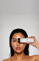 Close-up portrait of a woman holding Zenagen Revolve Women's Shampoo, designed for fine and visibly thinning hair.
